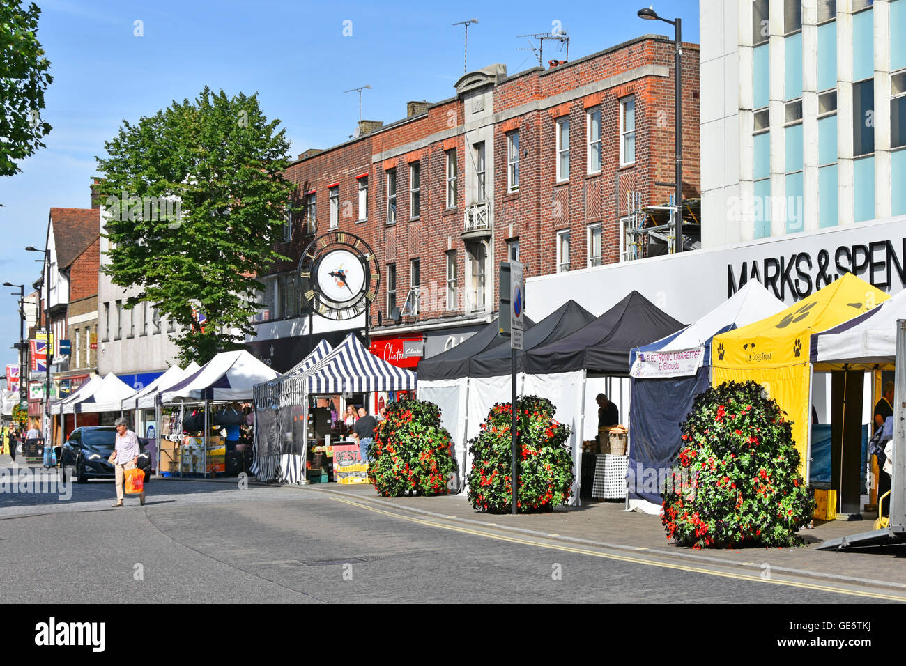 Englisches Stadtzentrum, Einkaufsmöglichkeiten, High Street-Geschäfte mit Marktständen vor Marks und Spencer, Sommerblumen und Stadtuhr Brentwood Essex UK Stockfoto