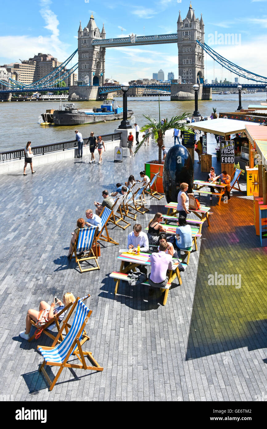 Touristen & Büroangestellte einrichten Mittagszeit an Fast-Food-Ständen für alfresco Snacks Sommer Liegestühle neben River Thames Tower Bridge UK jenseits Stockfoto