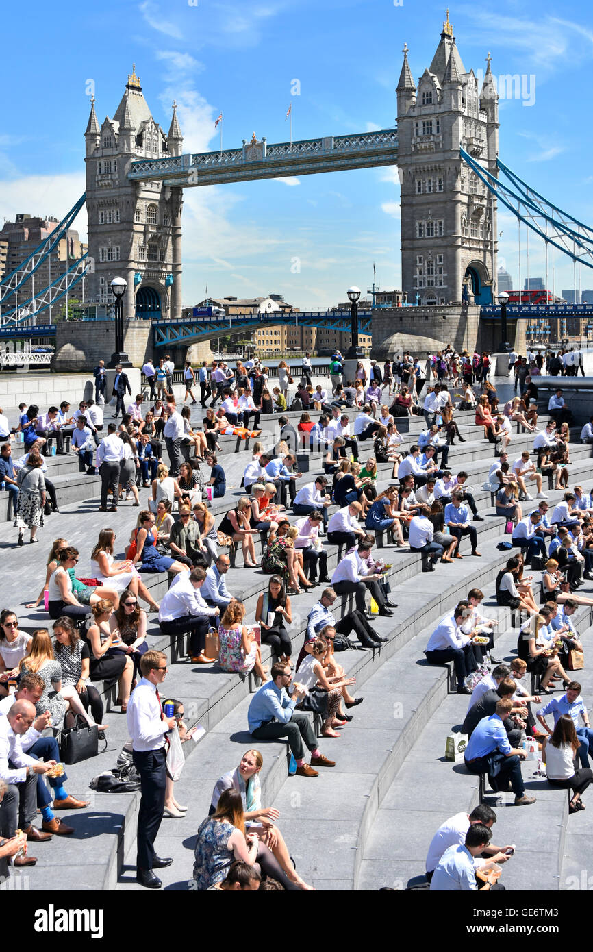 Heißer Tag für Büroangestellte & Touristen im Sommer mittags Pause rund um "The Scoop" Amphitheater London Tower Bridge England UK auf Themse über Stockfoto