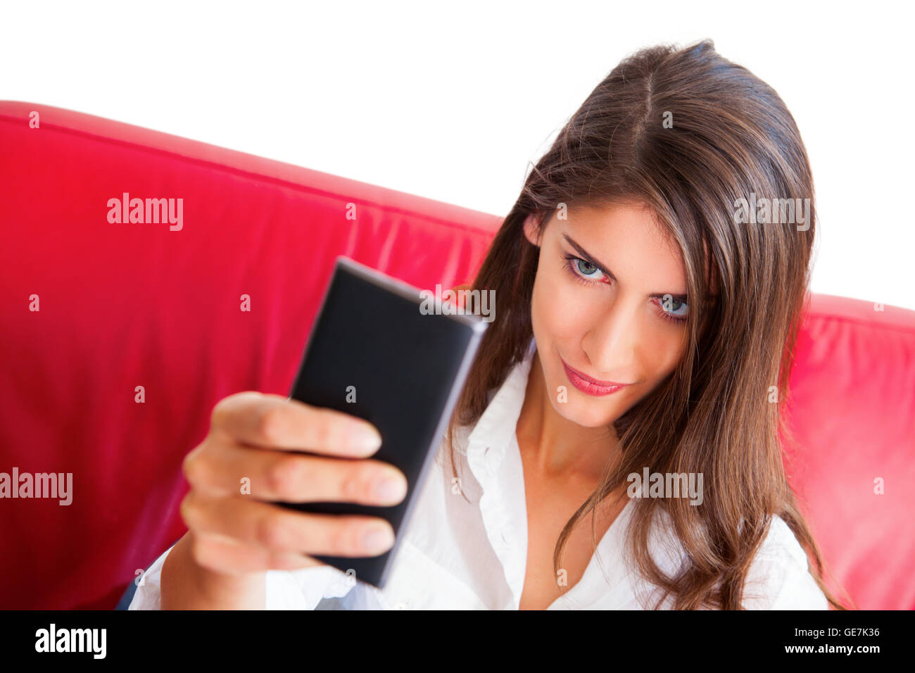 Junge Frau nehmen Selfie. Schöne Frau mit zuversichtlich Blick auf ihrem Gesicht halten Smartphone. Sie sitzt auf dem roten sofa Stockfoto