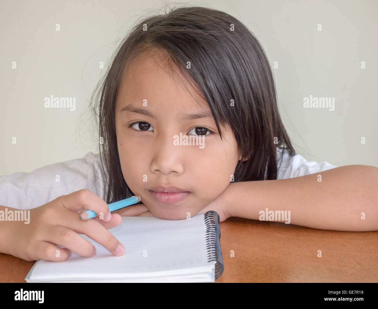 Kleine Asiatin schreiben mit Bleistift auf den Holztisch sitzend Stockfoto