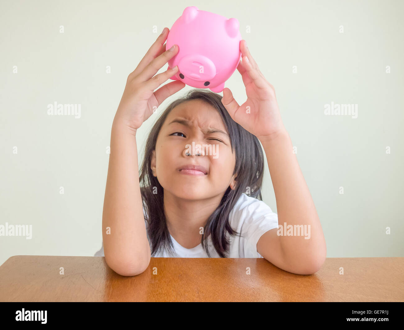 Kleine Asiatin sitzen auf den hölzernen Tisch und finden Sie ihr Geld für das Sparschwein. Stockfoto