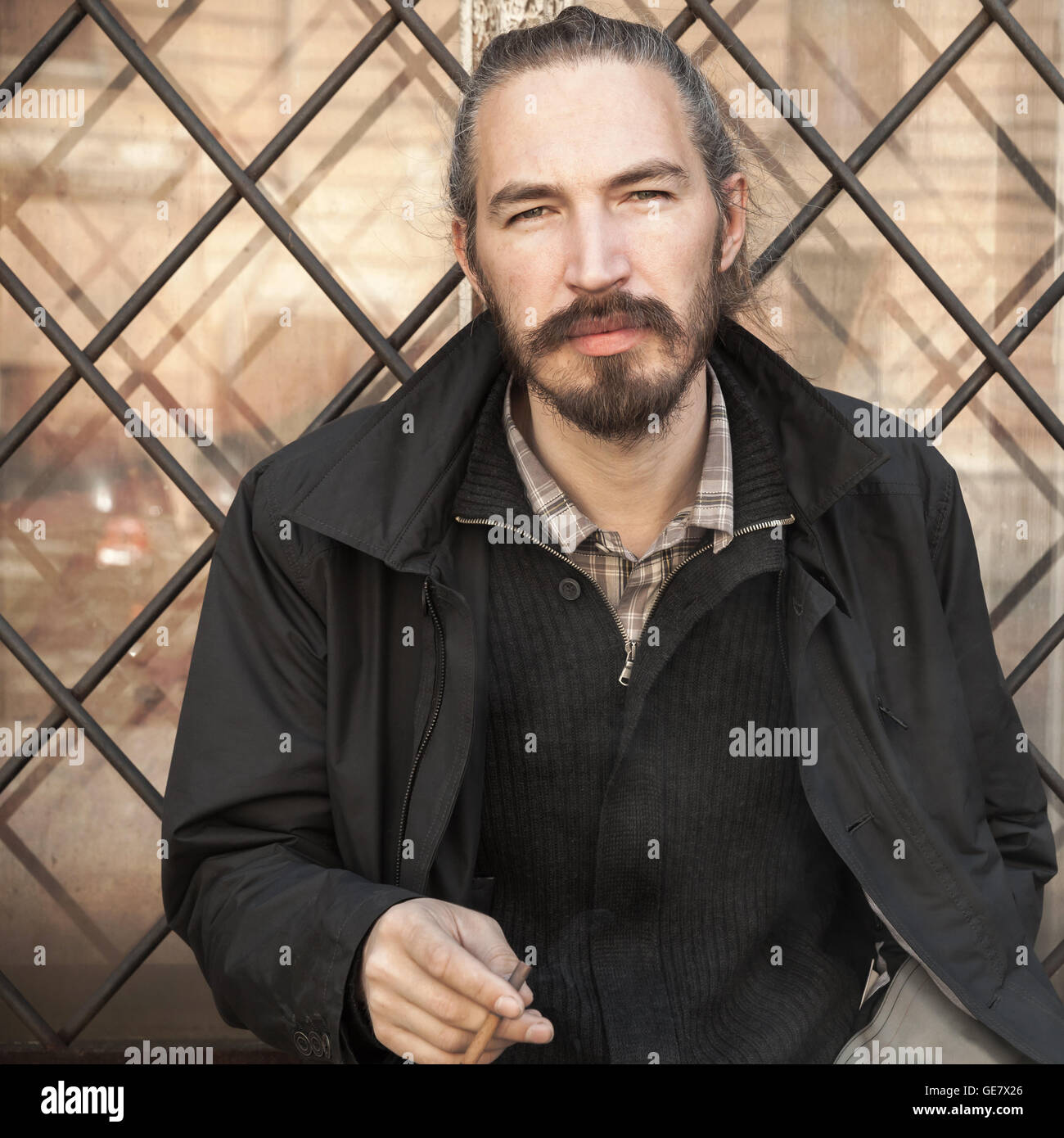 Bärtiger Mann rauchen Zigaretten, Outdoor-quadratische Porträt über Grunge Hintergrund mit selektiven Fokus Stockfoto