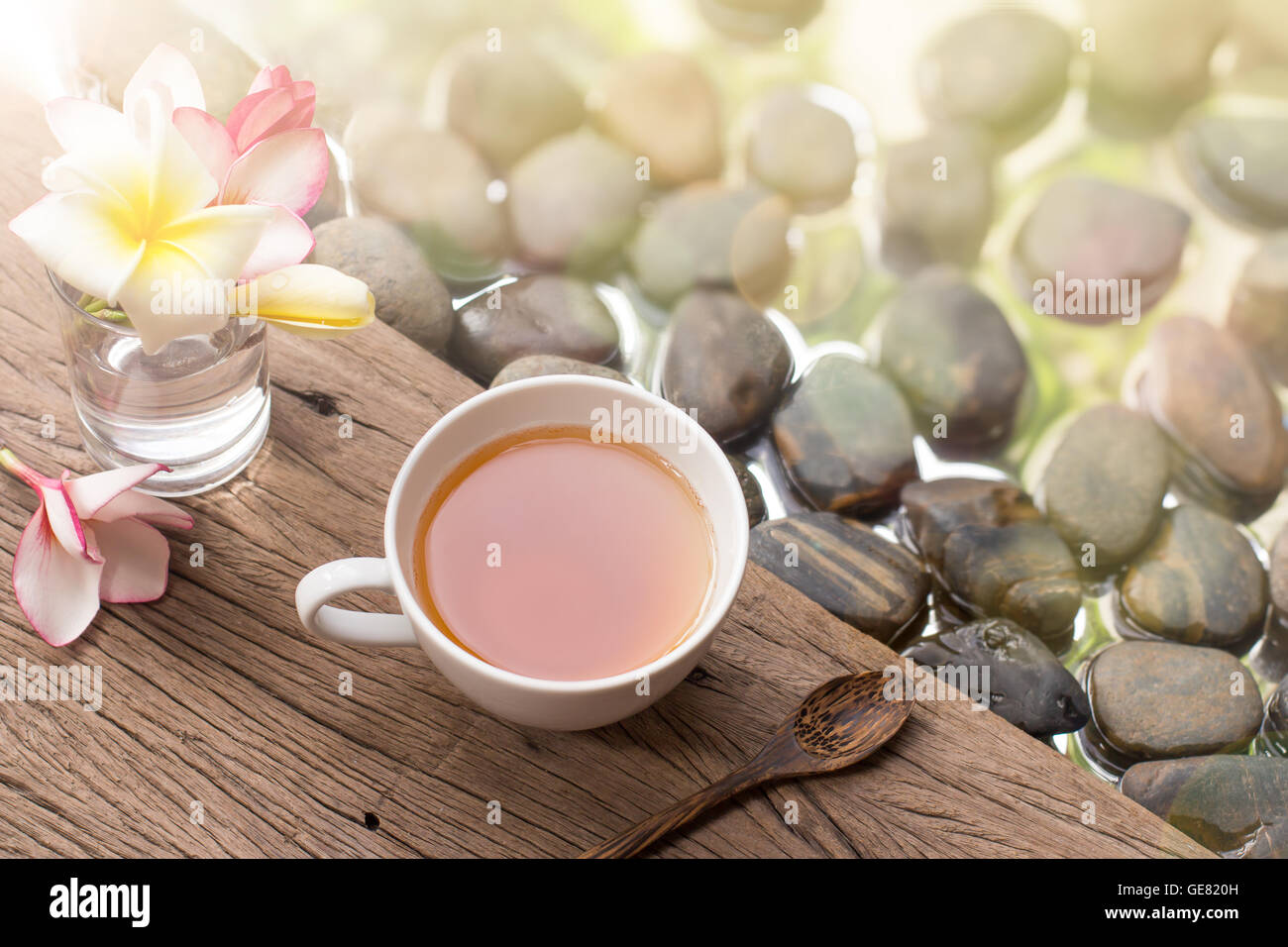 heißen Tee in weiße Tasse mit Blumen auf hölzernen Kiesel Stein Wasser Hintergrund Stockfoto