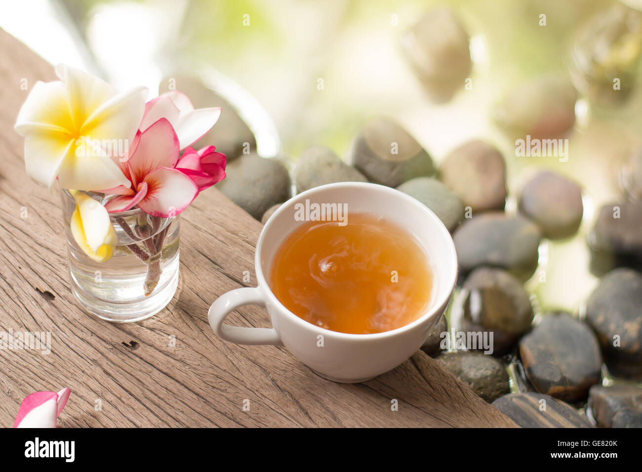 heißen Tee in weiße Tasse mit Blumen auf hölzernen Kiesel Stein Wasser Hintergrund Stockfoto