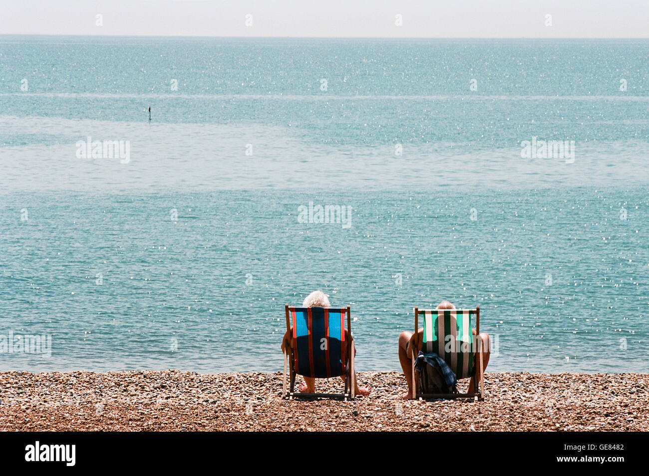 Ein paar sitzt in Liegestühlen am Strand von Hastings, East Sussex UK, im Juli Stockfoto