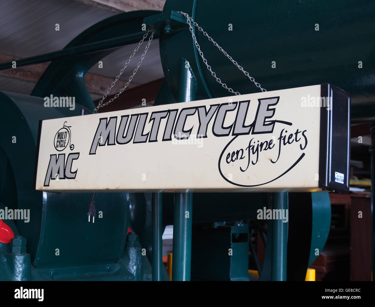 Dieses Bild zeigt eine Werbung für MC Multicycle auf einem Leuchtkasten. Der Vintage-Werbespot spiegelt das Werbedesign des frühen 20. Jahrhunderts wider und hebt die Fahrradmarke mit auffälligen, klaren Schriften und einem Schwerpunkt auf Fahrradkultur hervor. Stockfoto