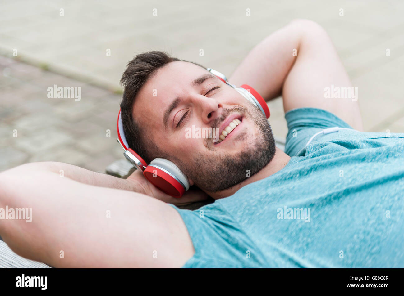 Entspannte junger Mann auf Bank Musikhören liegend Stockfoto