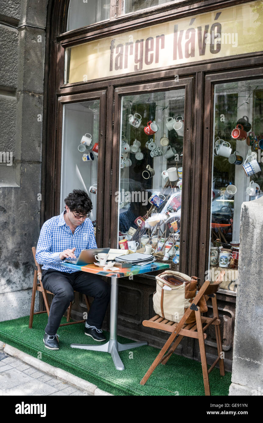 Ein Büroangestellter, der mit seinem Laptop vor einem Café in Budapest, Ungarn Stockfoto