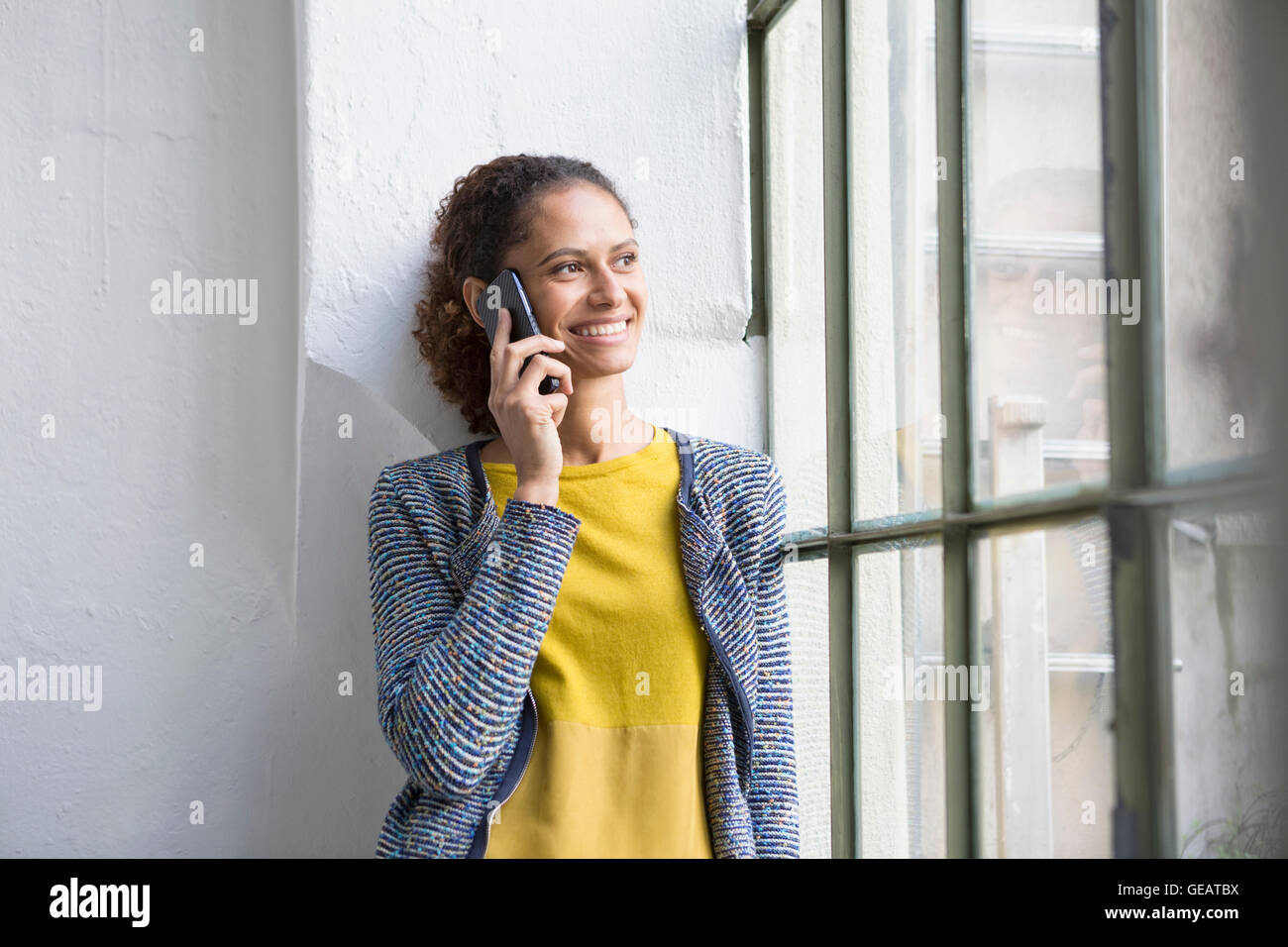 Junge Frau am Fenster stehend, am Telefon sprechen Stockfoto