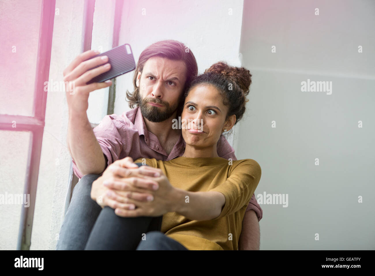 Junges Paar sitzt auf der Fensterbank unter Selfie mit Smartphone Stockfoto