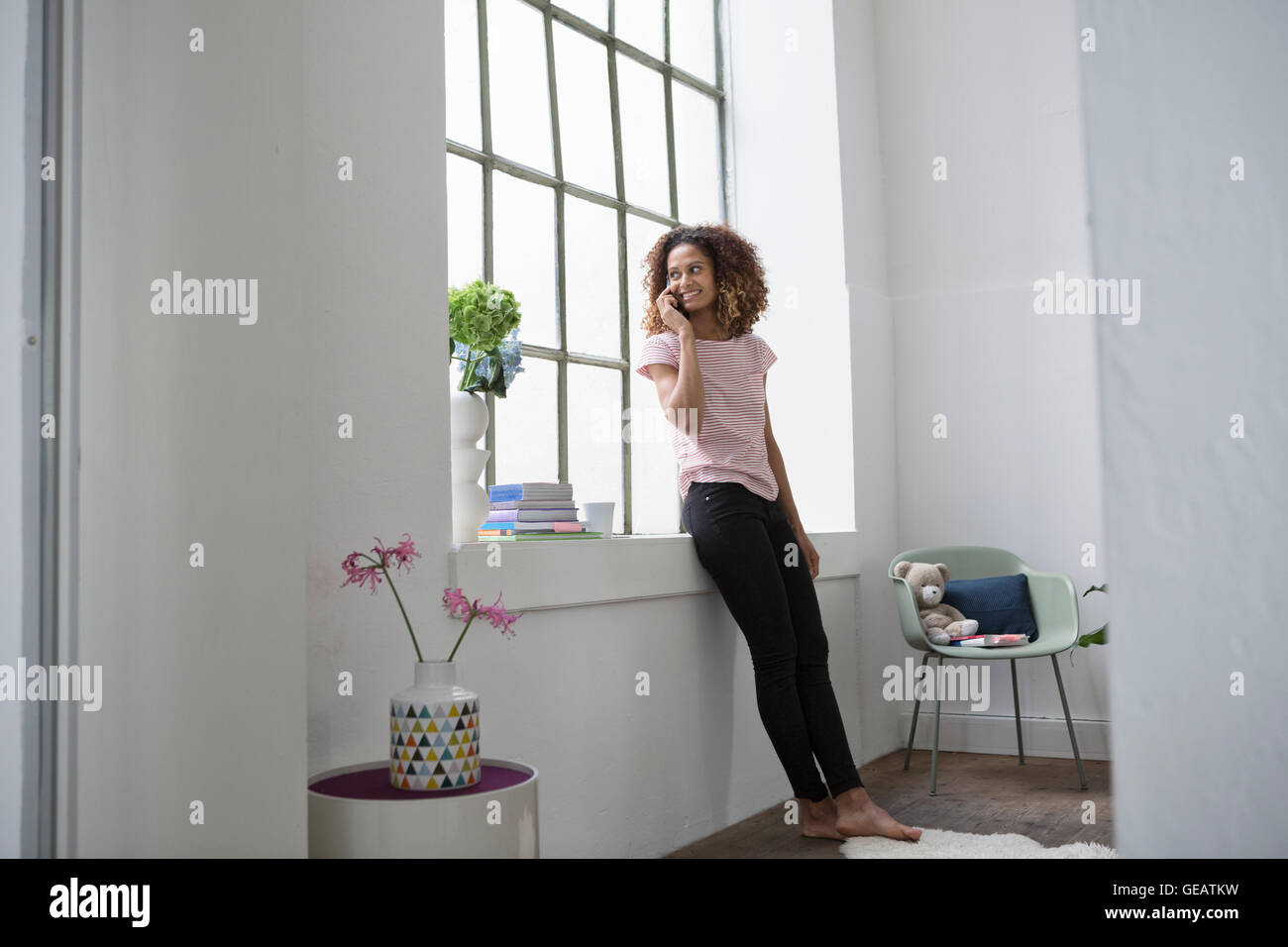 Junge Frau steht am Fenster telefonieren Stockfoto