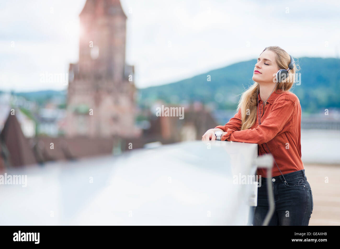 Deutschland, Saarbrücken, Frau Musik hören mit Kopfhörern auf Dachterrasse Stockfoto