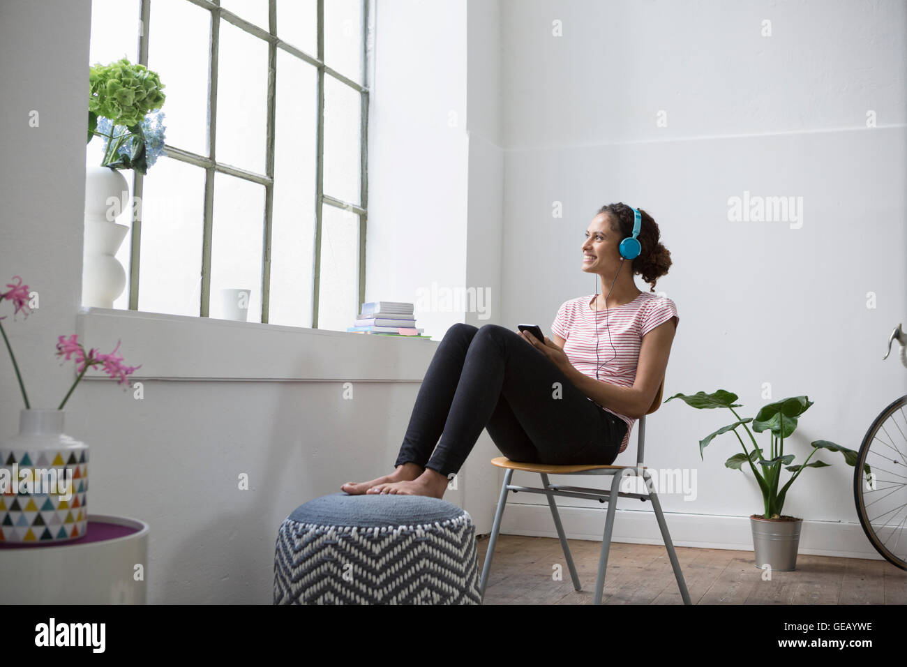 Junge Frau sitzt auf dem Stuhl Musik hören mit Kopfhörern Stockfoto