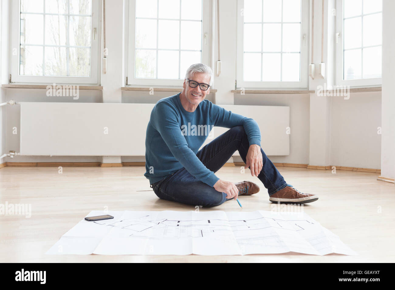Porträt von lächelnden Mann mit Bauplan in leerstehenden Wohnung Stockfoto