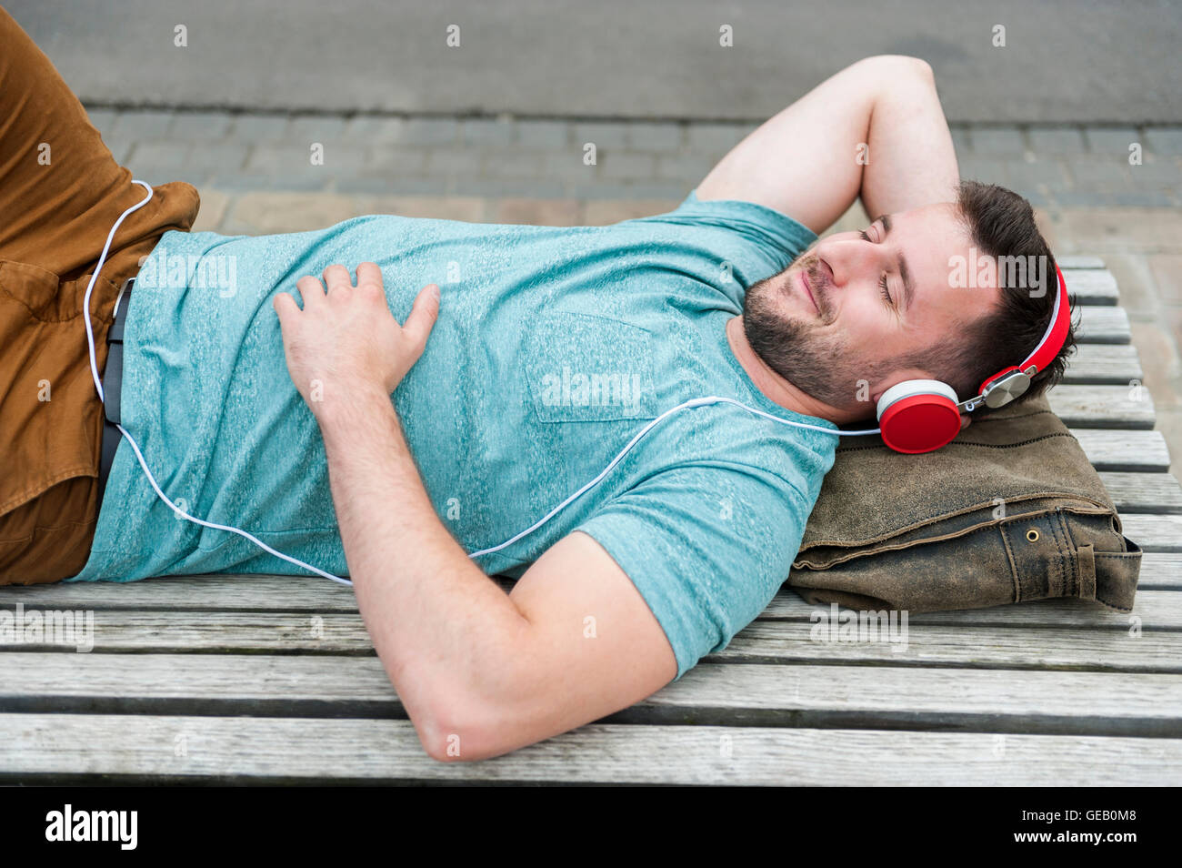 Entspannte junger Mann auf Bank Musikhören liegend Stockfoto