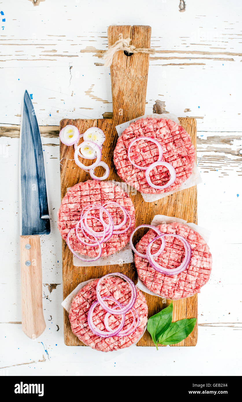 Rohen Boden Rindfleisch Fleisch Schnitzel, Burger mit Zwiebelringen und Gewürzen auf Holzbrett über weiße Zeitmessung Stockfoto