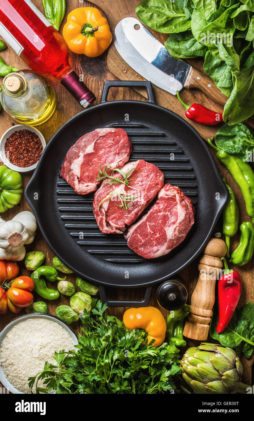 Zutaten für gesundes Fleisch Abendessen kochen. Rohes Rindfleisch Steaks  mit Gemüse, Reis, Kräuter, Gewürze und Weinflasche über rustikalen  hölzernen Hintergrund Stockfotografie - Alamy