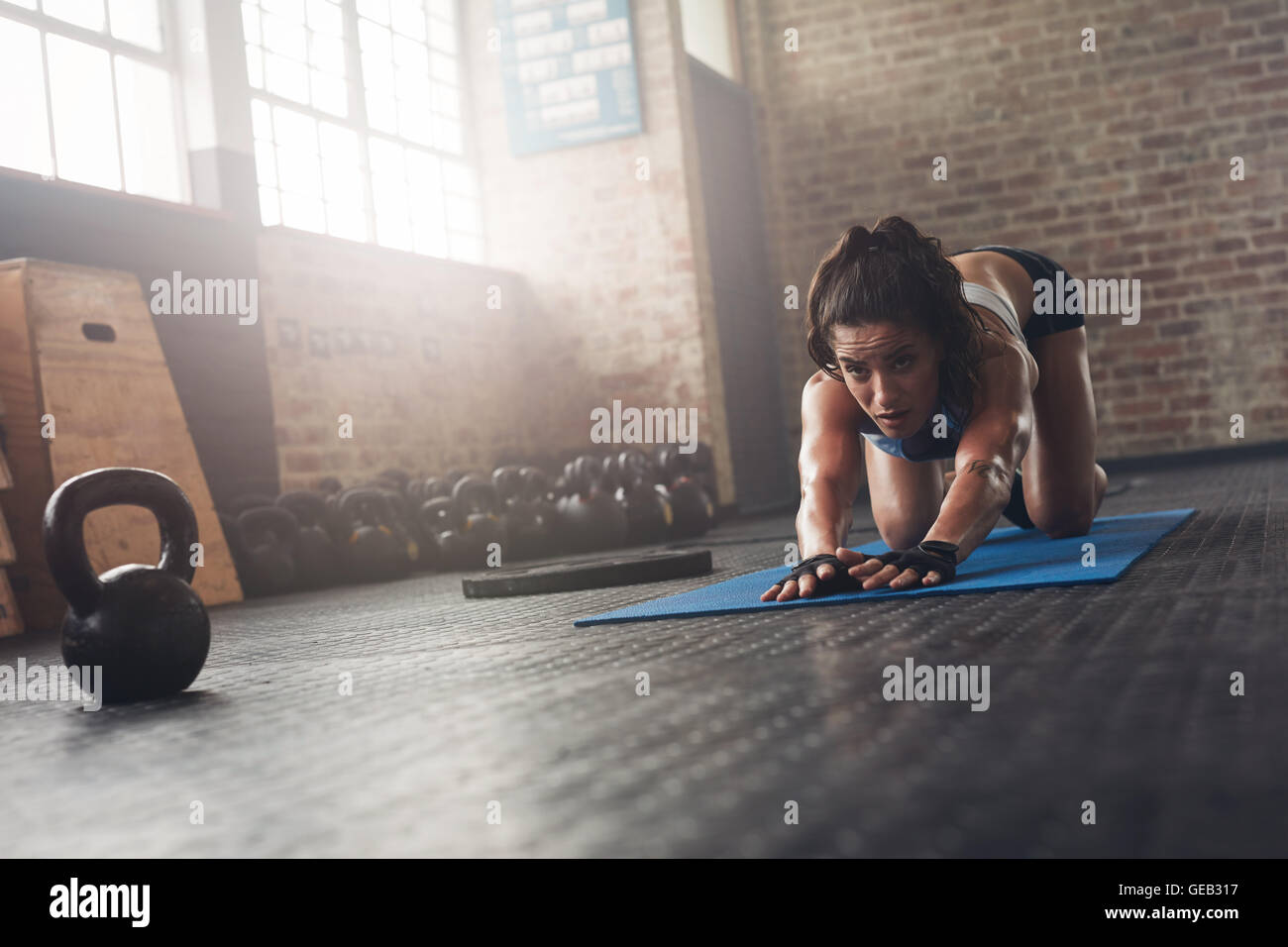 Porträt der entschlossene junge Sportlerin auf Trainingsmatte im Fitnessraum trainieren. Konzentrierte sich Frau stretching auf Fitness-Matte. Stockfoto