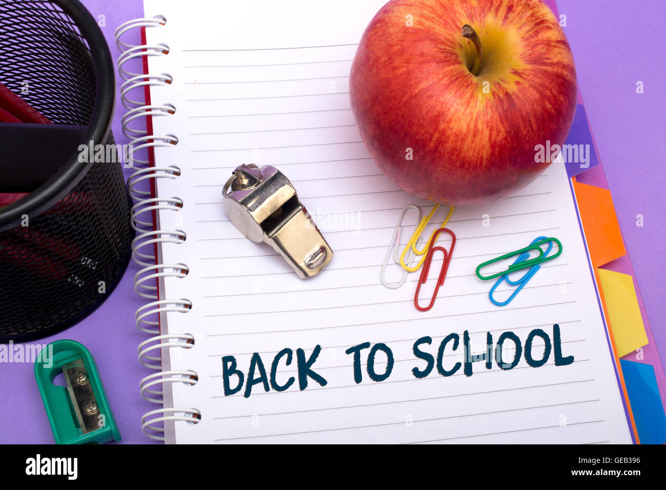 Schulmaterialien mit roter Apfel auf einem lila Hintergrund. Stockfoto