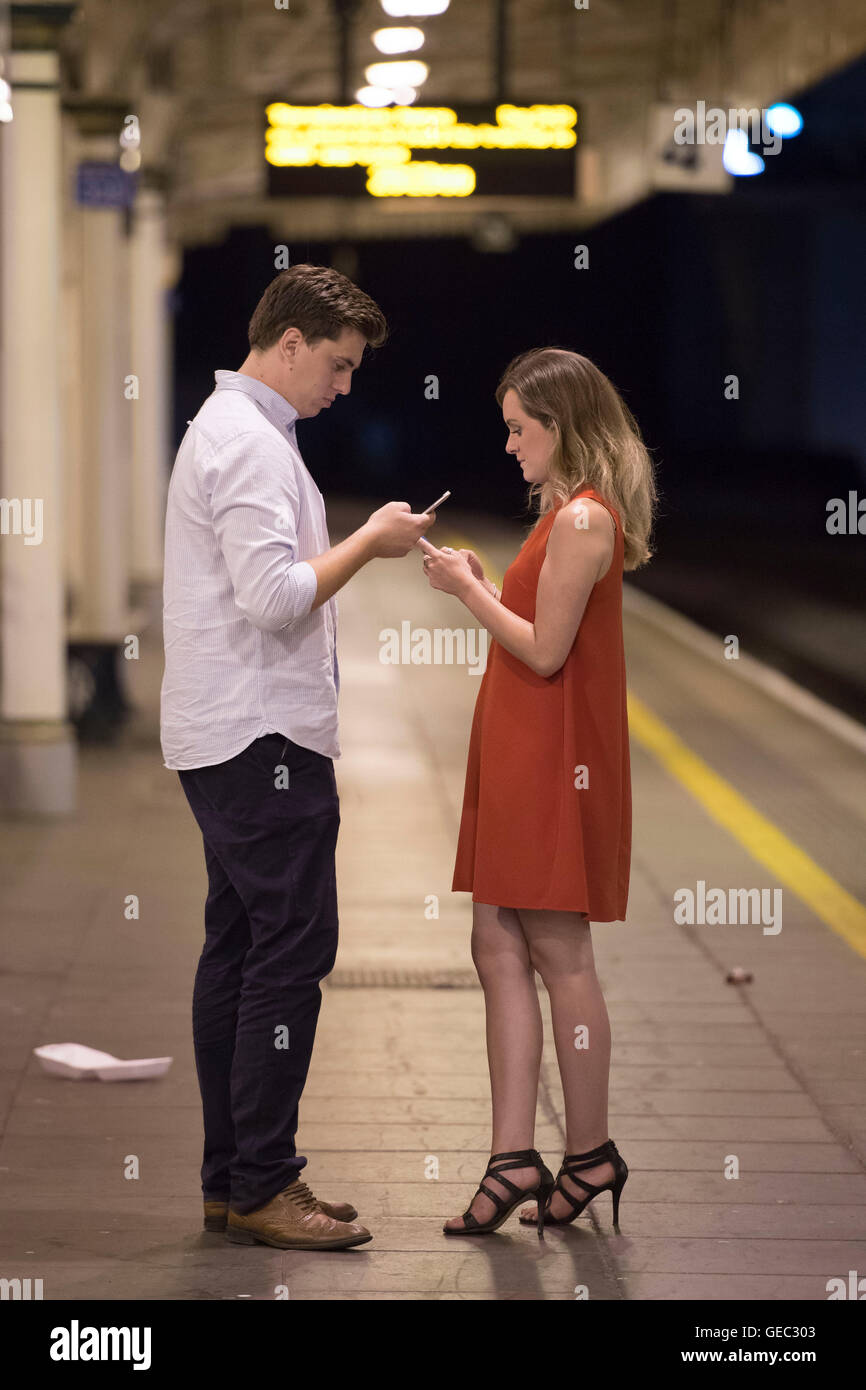 Mann und Frau SMS auf ihrem Handy unter Missachtung einander ein Bahnsteig ein Zug in der Nacht. Stockfoto