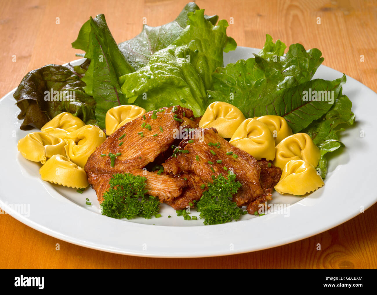 Gebratenes Huhn mit frischen grünen Salat und Tortellini Nudeln auf einem weißen Teller Stockfoto