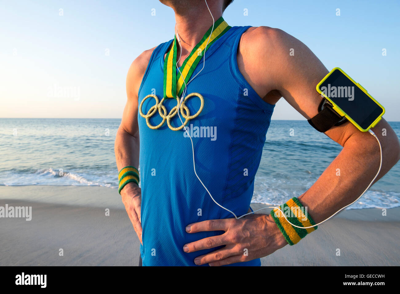RIO DE JANEIRO - 10. März 2016: Sportler der Olympischen Ringe gold Medaillen und Sport Armband steht an einem Sonnenaufgang Strand tragen. Stockfoto