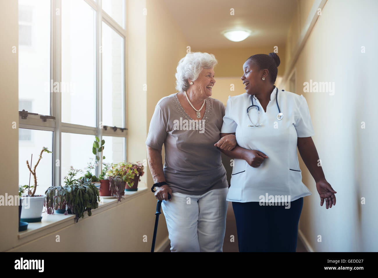 Porträt der lächelnde Mitarbeiter zu Fuß und mit älteren Frau zu reden. Glückliche ältere Frau bekommt Hilfe von Krankenschwester für einen Spaziergang-t Stockfoto