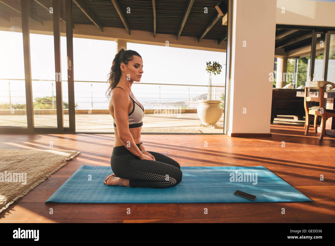 Seitenansicht einer schönen jungen Frau, die zu Hause in Yoga-Pose sitzt. Fitness-Frau, die Meditation auf der Trainingsmatte im Leben macht Stockfoto