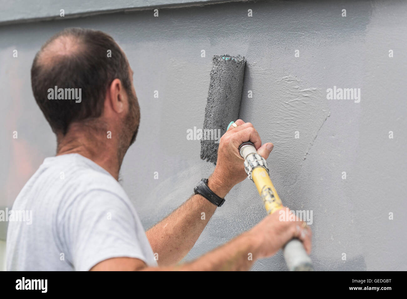 Ein Maler und Dekorateure, der mit einer Walze die Außenwand eines Hauses malt. Stockfoto