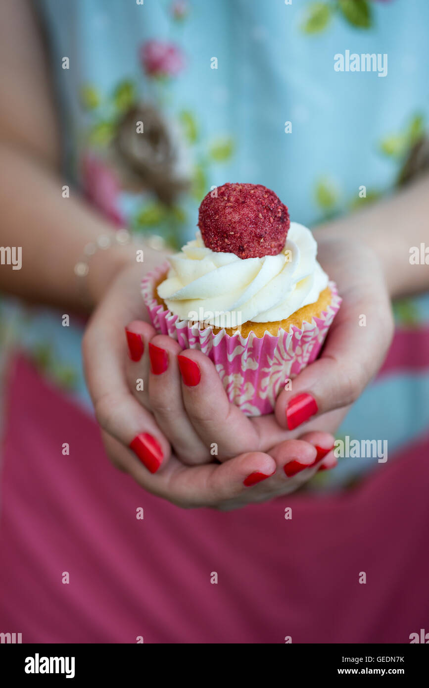 Frauenhand hält einen hübschen Cupcake garniert mit weißem Zuckerguss und Himbeere Stockfoto