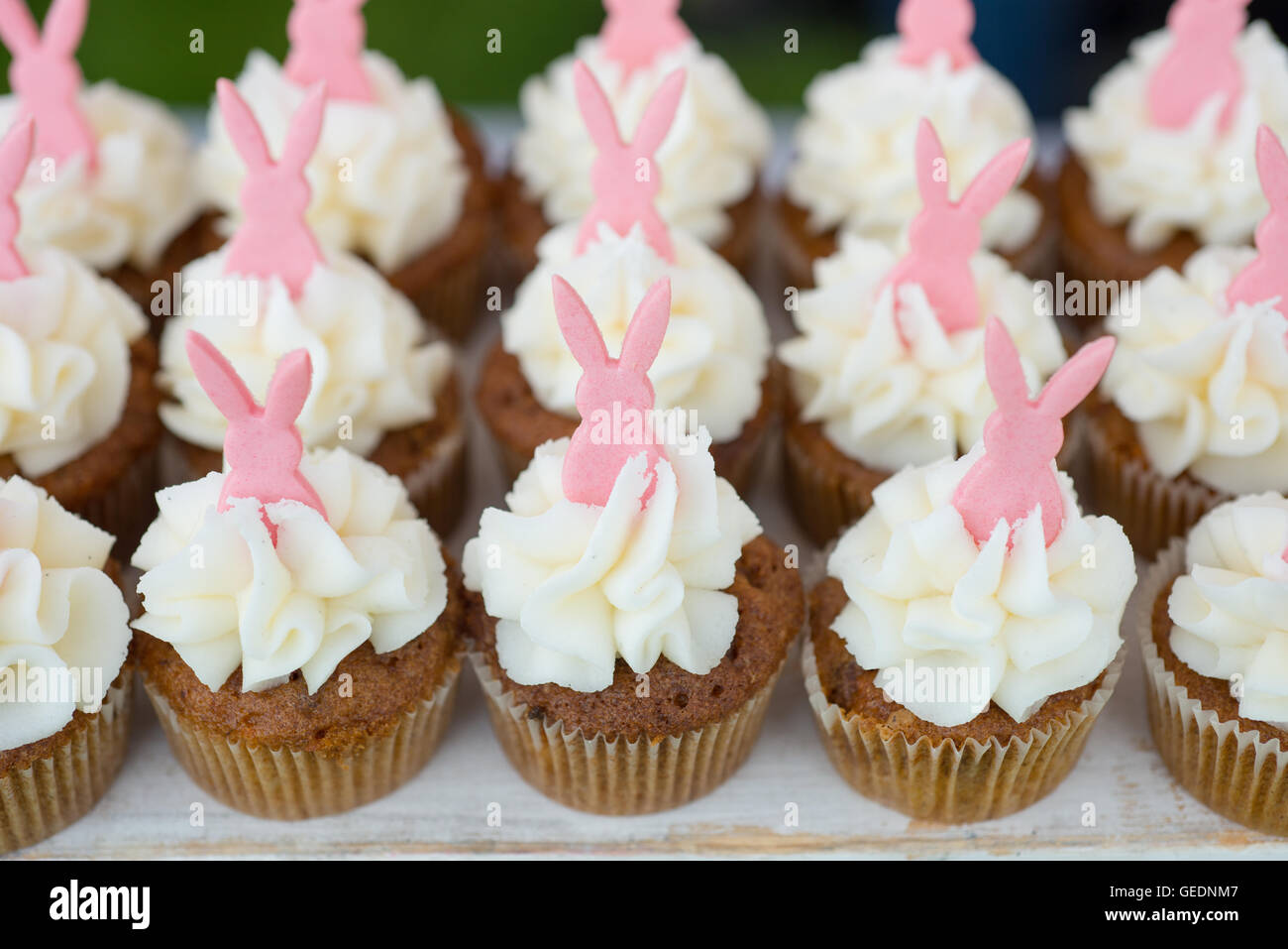 Reihen von Hand verziert-Cupcakes mit weißer Glasur verrohrt und rosa Hasen an der Spitze Stockfoto