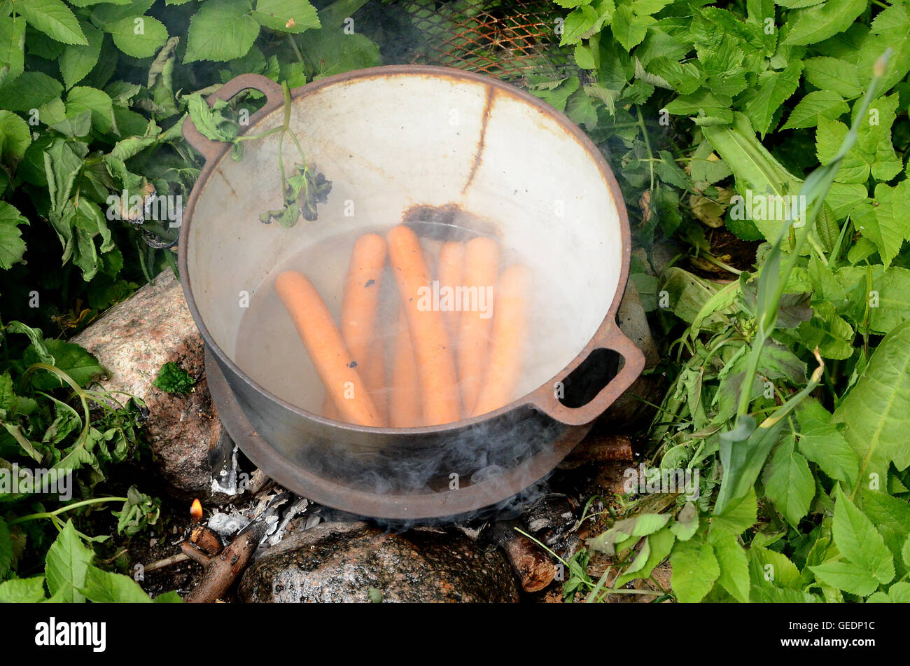 Bockwurst Würstchen in einem gerissenen Gusseisen Topf über dem offenen Feuer erwärmt wird. Stockfoto