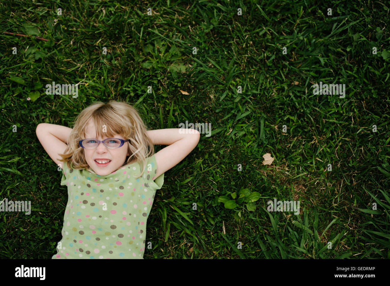 Junges Mädchen mit Brille, die Verlegung auf dem Rasen, High Angle View Stockfoto