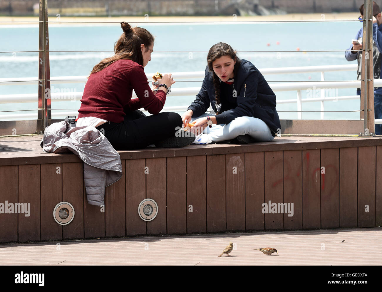 Zwei junge Frauen Mädchen Sandwiches Essen und füttern Spatzen in San Sebasti‡n Donostia, Spanien Stockfoto