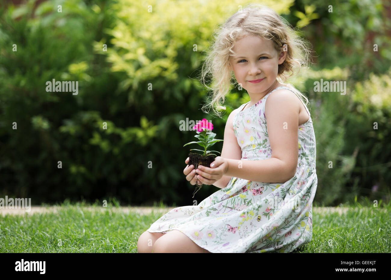 Kleine blonde Mädchen halten junge Blume Pflanze in die Hände auf grünem Hintergrund Stockfoto