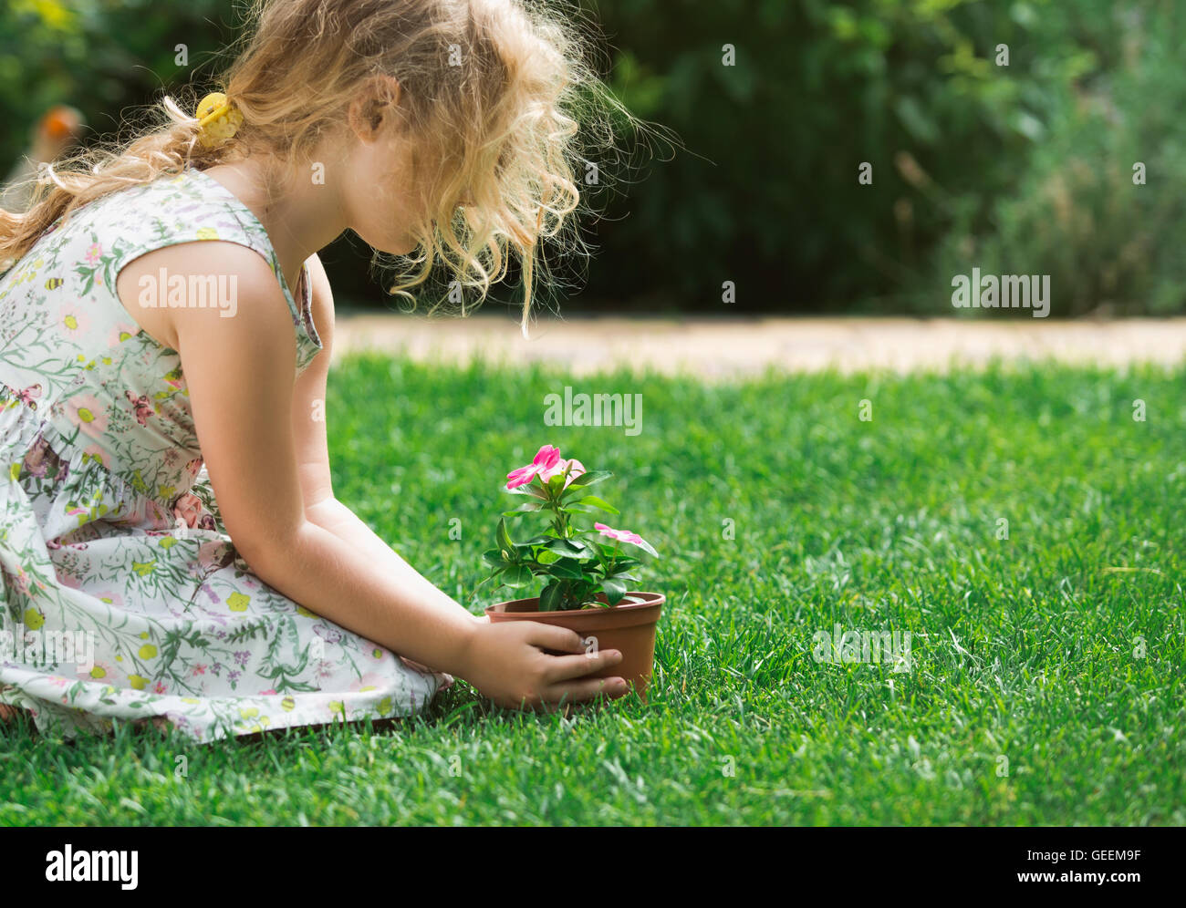 Kleine blonde Mädchen halten junge Blume Pflanze in die Hände auf grünem Hintergrund Stockfoto