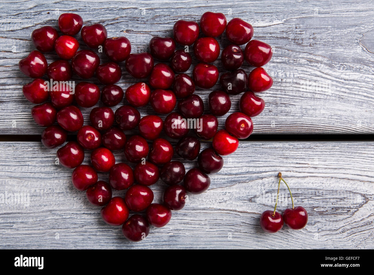 Herzen von dunklen Kirschen gemacht. Rote Früchte auf hölzernen Hintergrund. Sommer sendet Liebe. Partikel der Kunst. Stockfoto