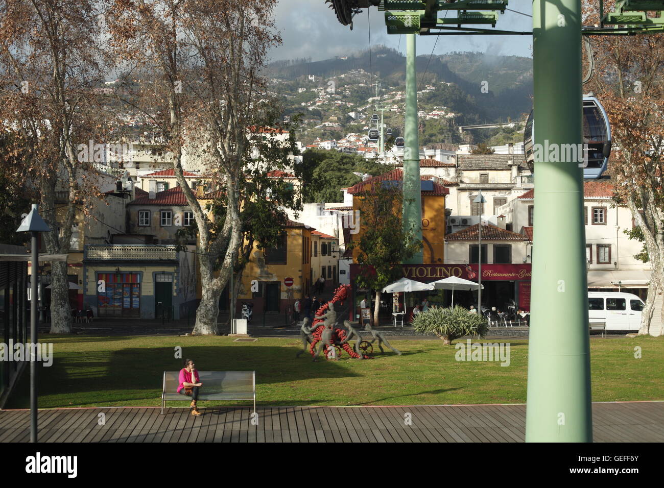 O Teleférico Funchal.  Eine Frau sitzt unterhalb der Seilbahn entfernt erhebt sich des Bergs von der Stadt Funchal, Madeira. Stockfoto