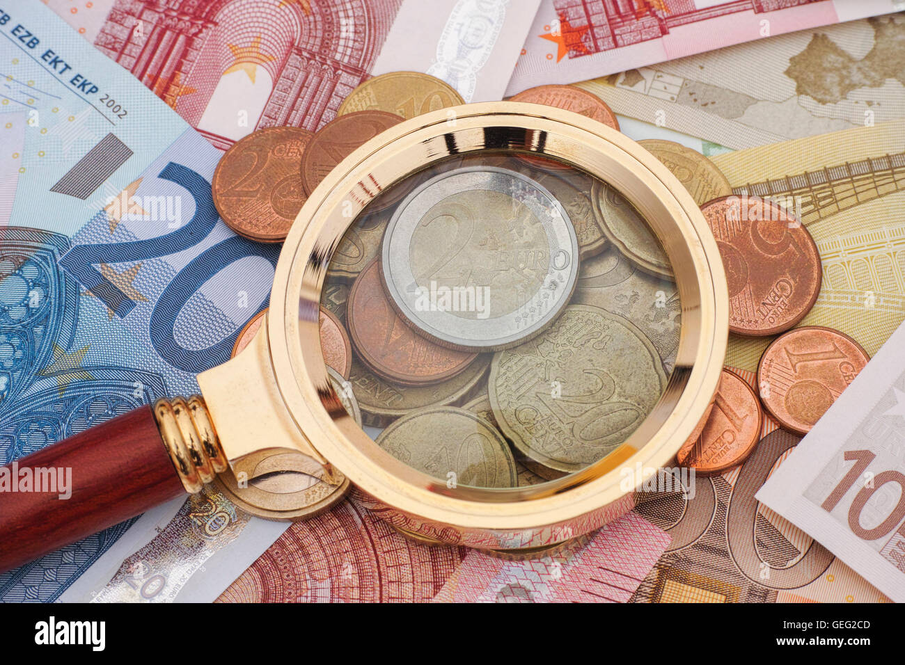 Lupe und Euro-Banknoten mit Münzen. Krisenkonzept. Stockfoto