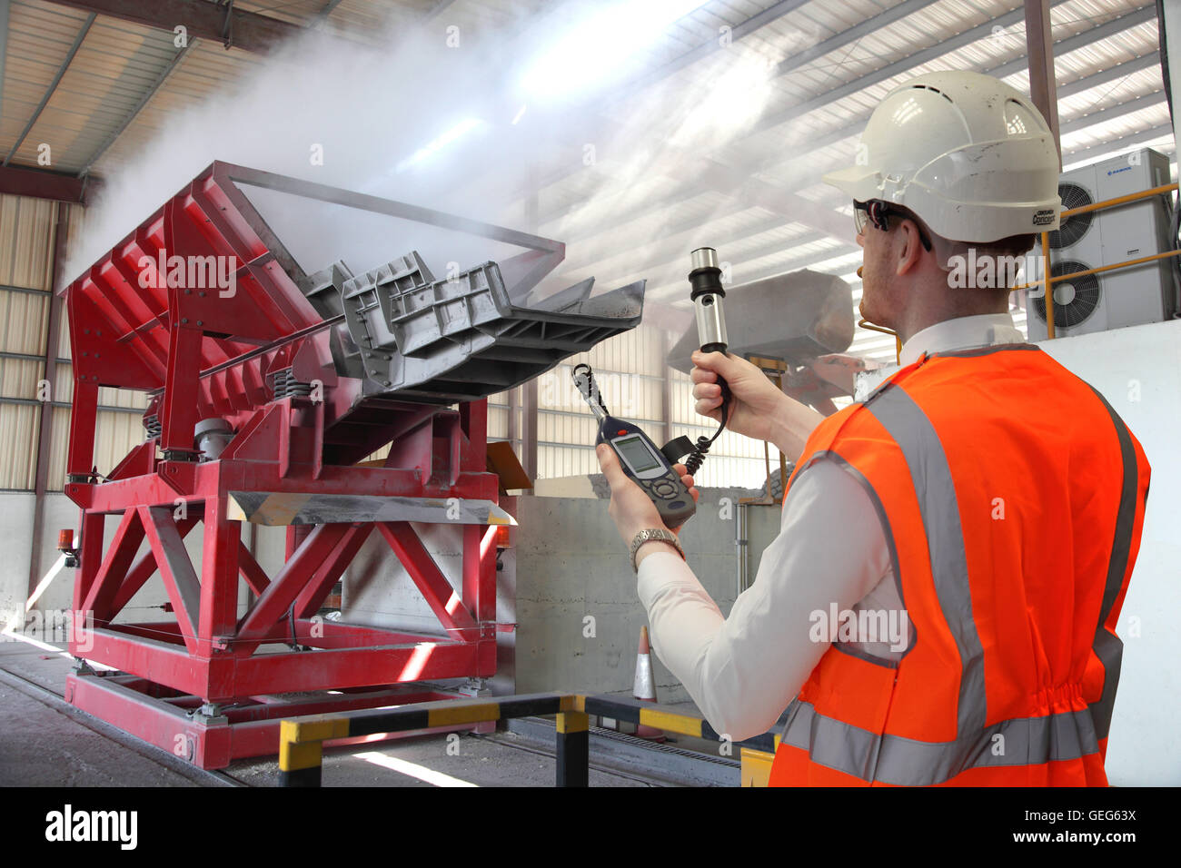 Ein Umwelt-Ingenieur überwacht Staubentwicklung neben einem Materialien Trichter auf einer Aluminium-Rückgewinnungsanlage. Fotomontage. Stockfoto
