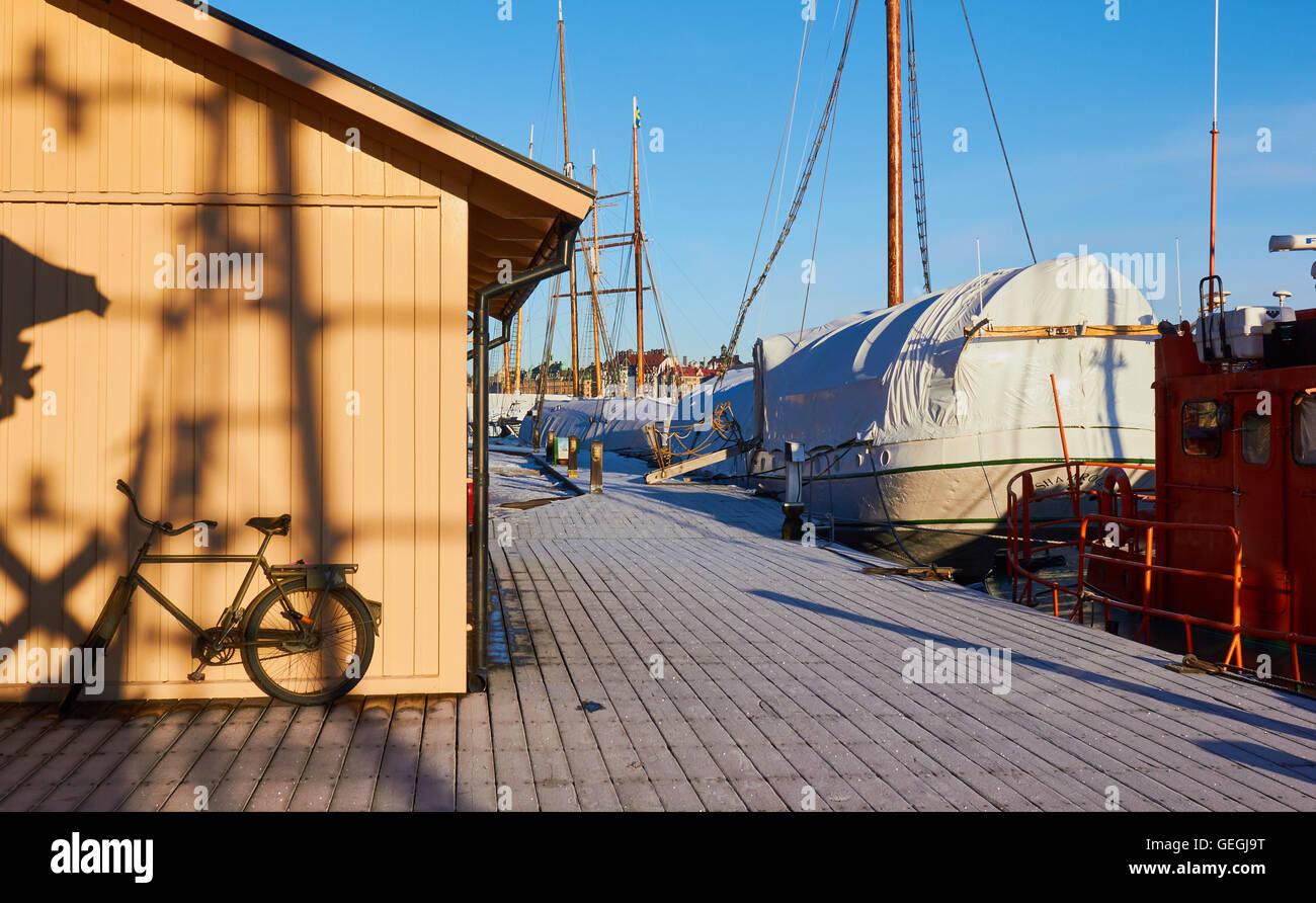 Fahrrad auf eisigen Boardwalk neben Holzhaus und angelegten Boote Insel Skeppsholmen Stockholm, Schweden Skandinavien Stockfoto