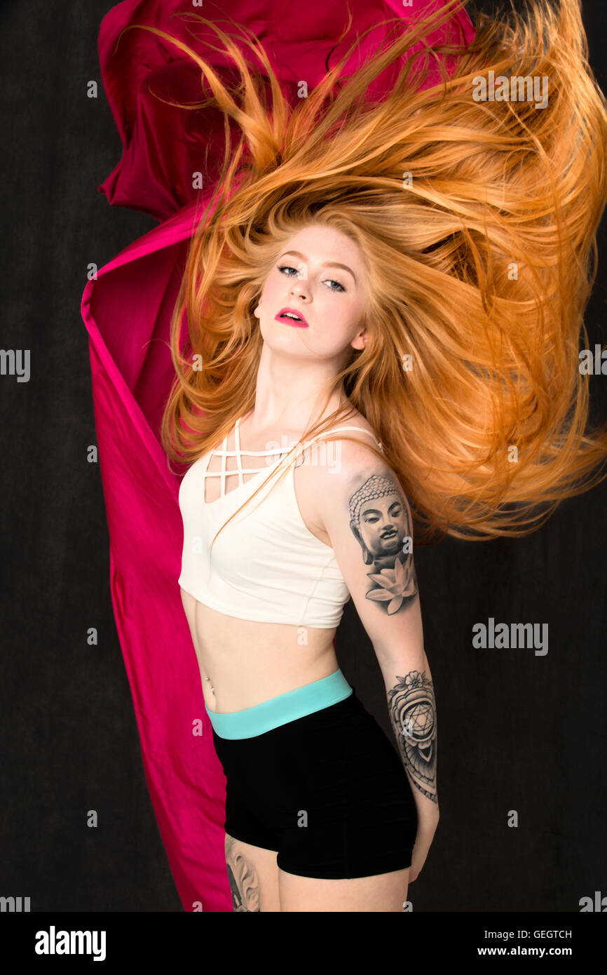 Junge Tänzerin, deren langes rotes Haar, hinter ihr mit rotem Stoff ausgesetzt neben ihr strömt. Stockfoto