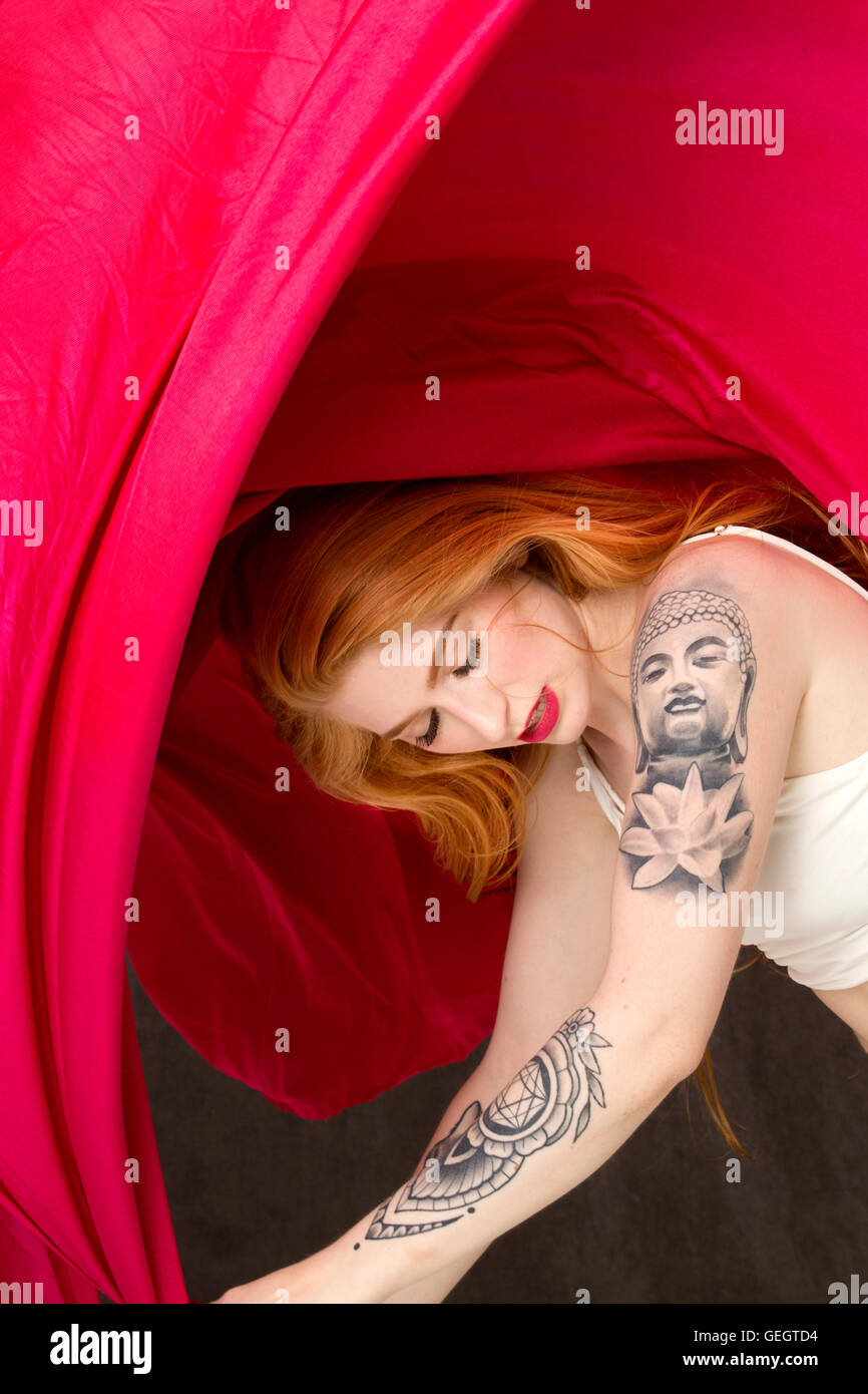 Junge Frau Tänzerin mit tattoos biegen sich unter einem Baldachin von Streaming-roten Stoff. Stockfoto