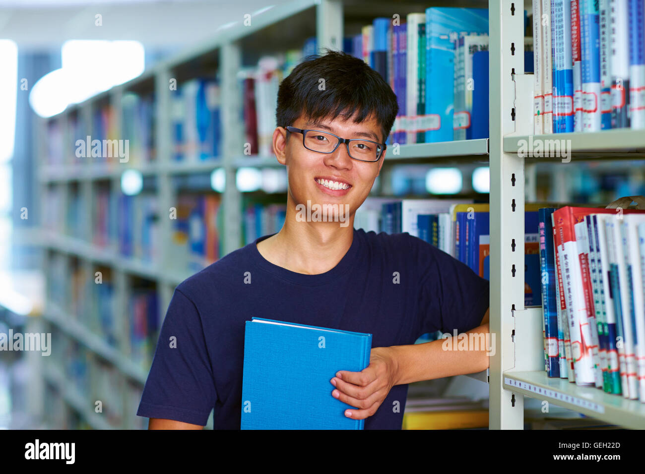 Eine junge männliche asiatische und chinesische Studenten Blick auf Kamera Lächeln in der Bibliothek Stockfoto