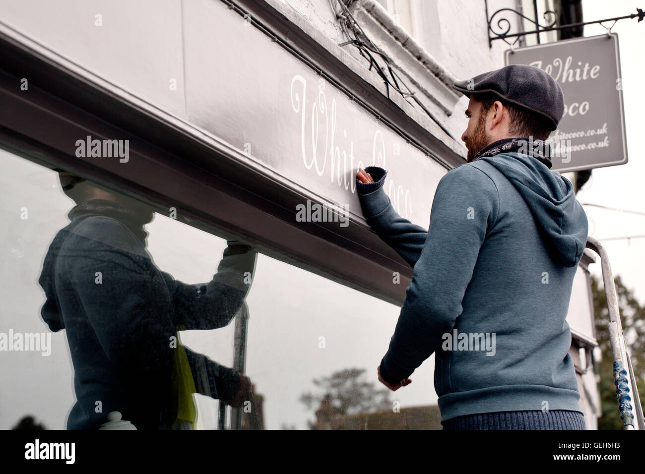 Ein Mann auf einer Leiter Befestigung eine gemalte Namensschild auf einer Halterung an einer Shops. Stockfoto