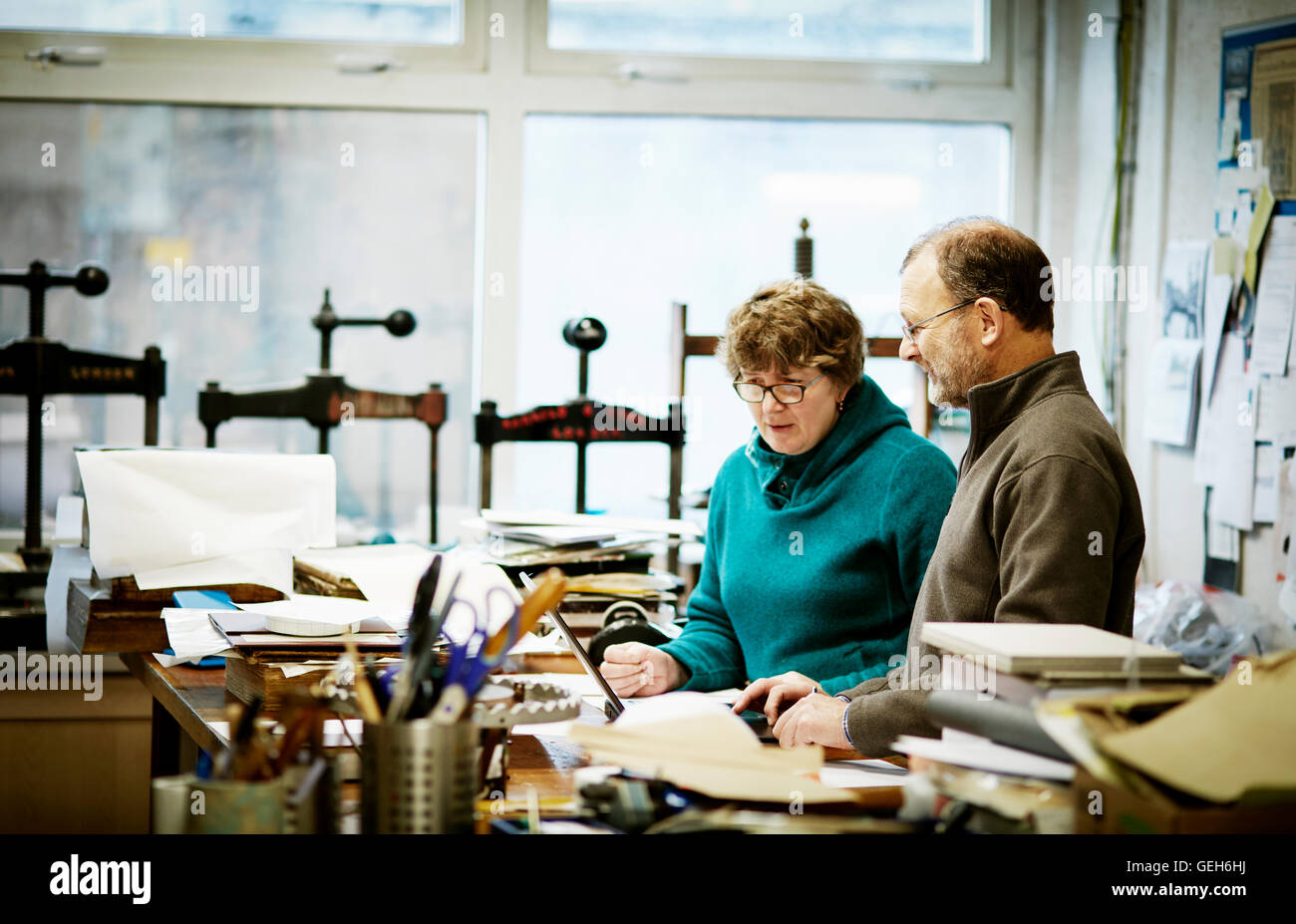 Zwei Personen in einem Buch Bindung Unternehmen arbeiten. Umgeben von Werkzeugen und Buch Pressen. Stockfoto