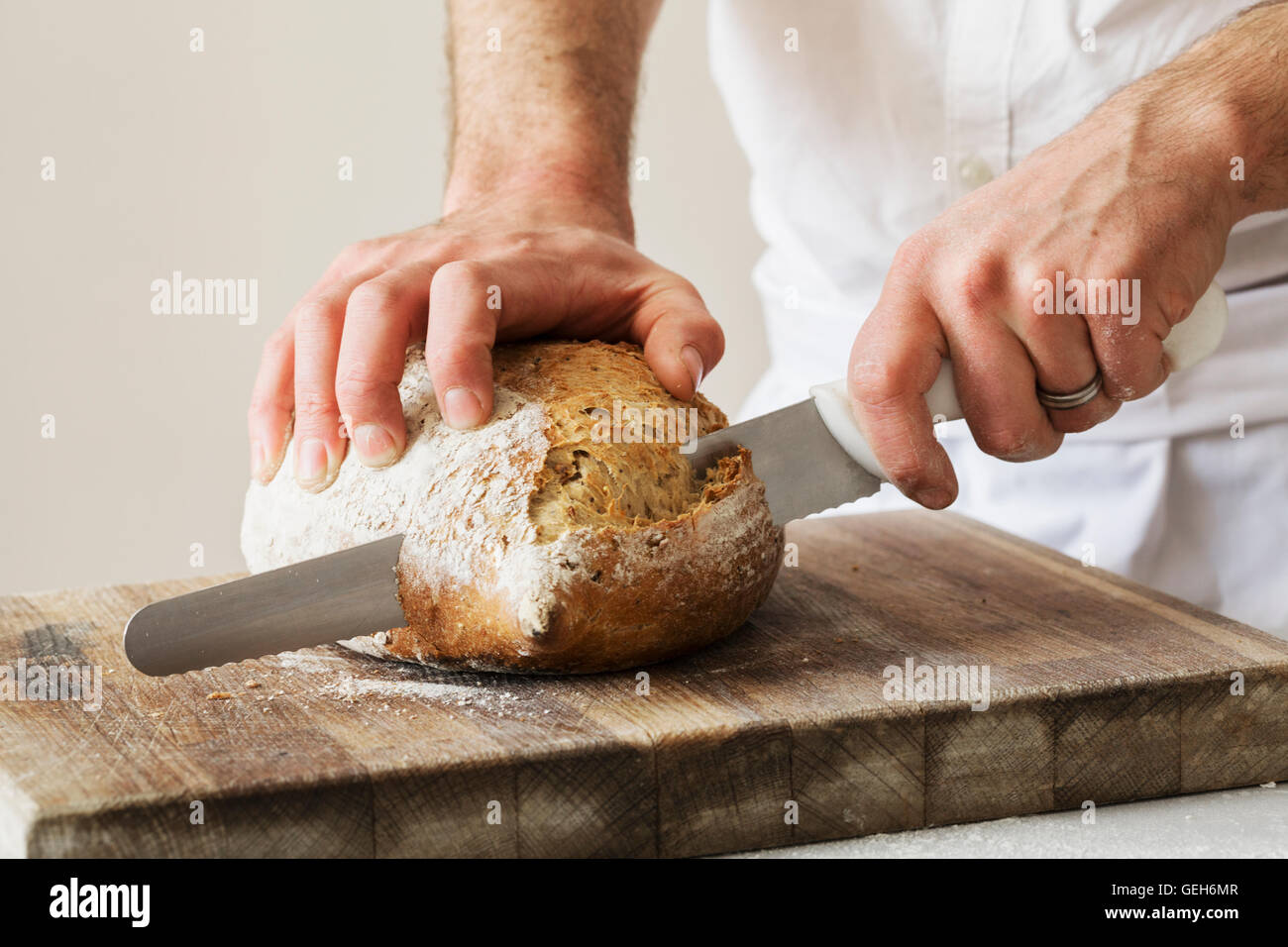 Nahaufnahme eines Bäckers ein frisch gebackenes Brot mit einem Brotmesser aufschneiden. Stockfoto