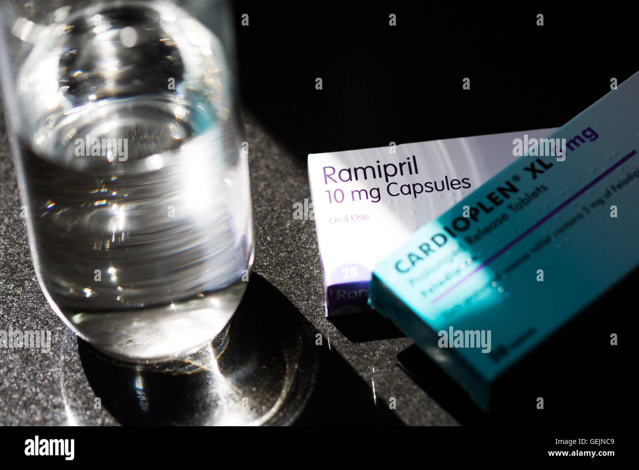 2 Boxen von Tabletten für hohen Blutdruck und ein Glas Wasser auf eine Arbeitsplatte Stockfoto