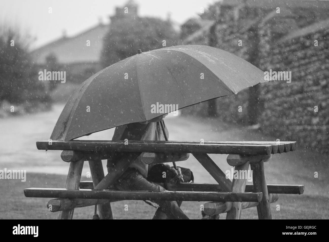Mann sitzt auf einer Bank unter einem großen Dach, während es stark regnet Stockfoto
